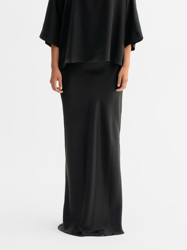 Model wearing Ahlvar Gallery Hana long logo satin skirt in Black